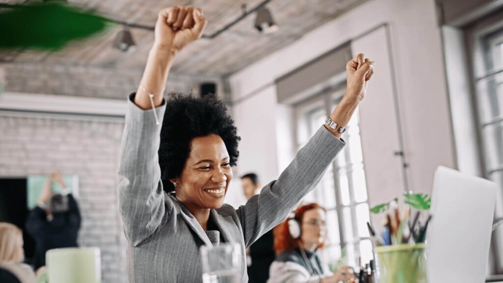 multisite certification - a woman cheering at work at her desk