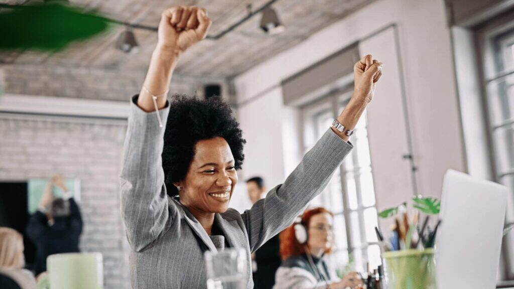 multisite certification - a woman cheering at work at her desk