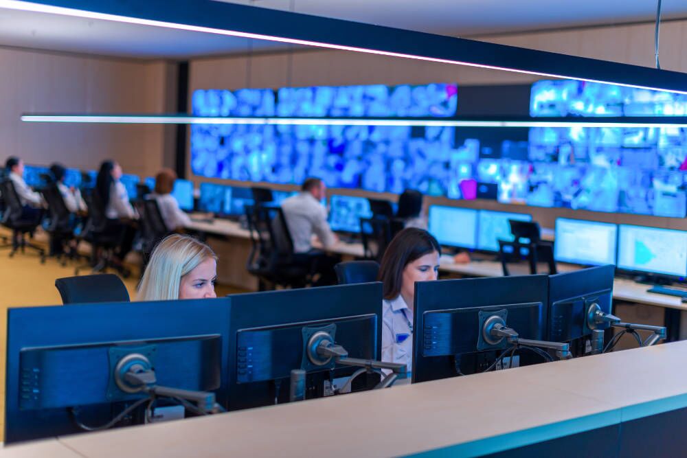 Amtivo (Formerly Certification Europe and EQA) - CCTV Monitoring - A wide view of a CCTV receiving centre with multiple screens showing footage.